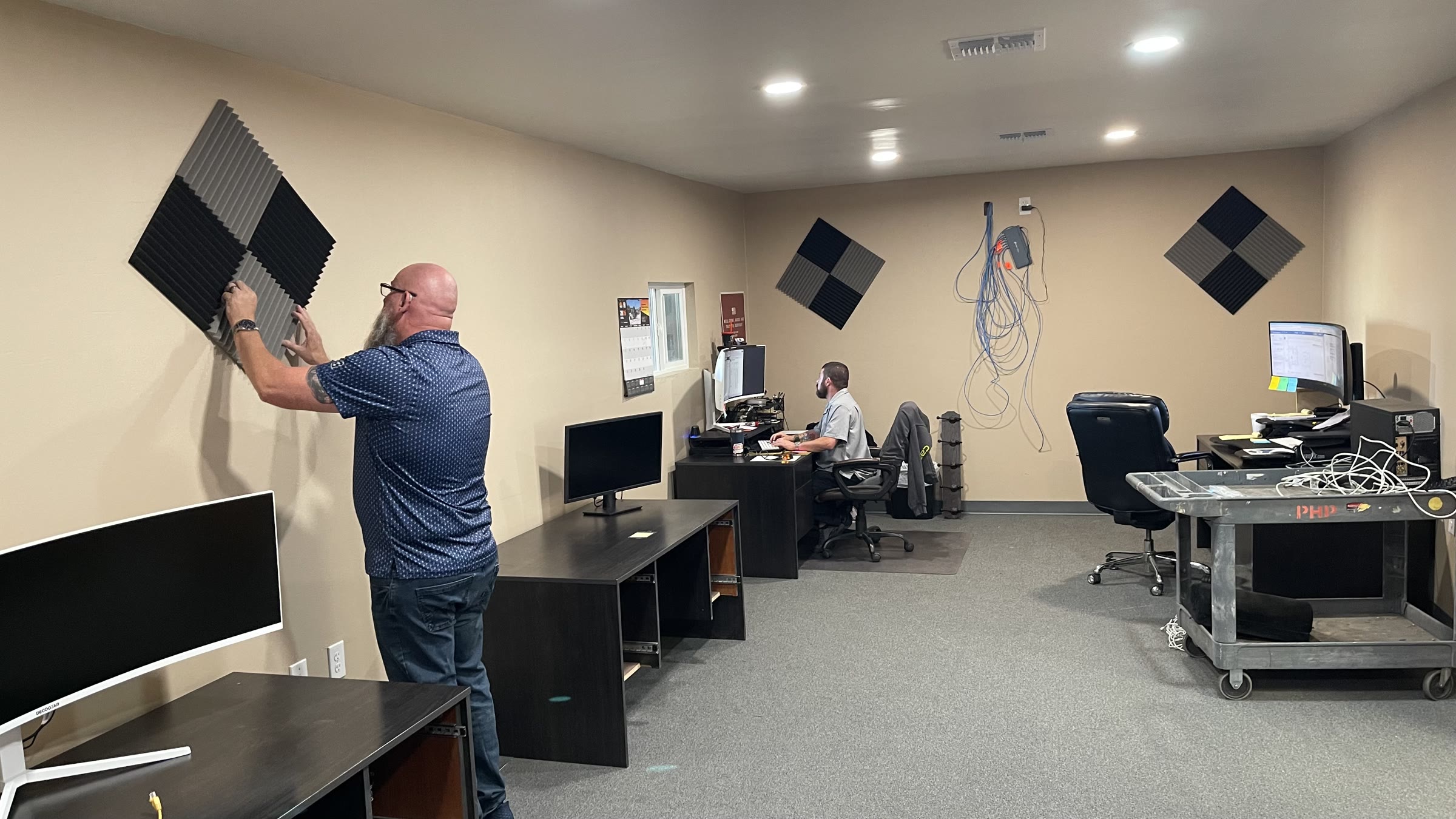 John Morris installing an acoustic panel in PHP’s new Estimating Office while Michael Nightingale works at his desk